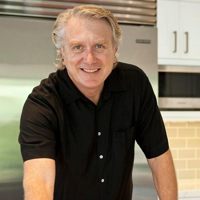 A man in black shirt standing next to a kitchen.